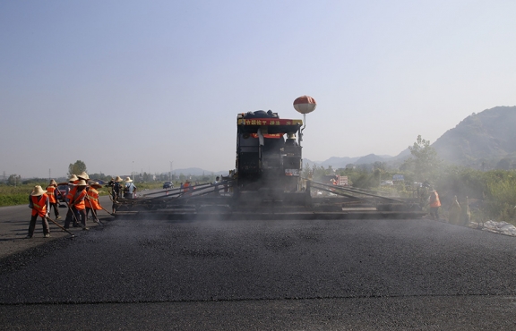 2019年8月，宜春經(jīng)開區(qū)S311路面攤鋪現(xiàn)場，工友們輔助路面兩側(cè)的分料、補(bǔ)窩等作業(yè)